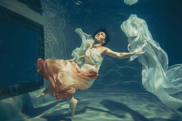 elegante slanke meisje zwemt onder water als een vrije duiker in een witte avondjurk met mooie stof - Foto, afbeelding