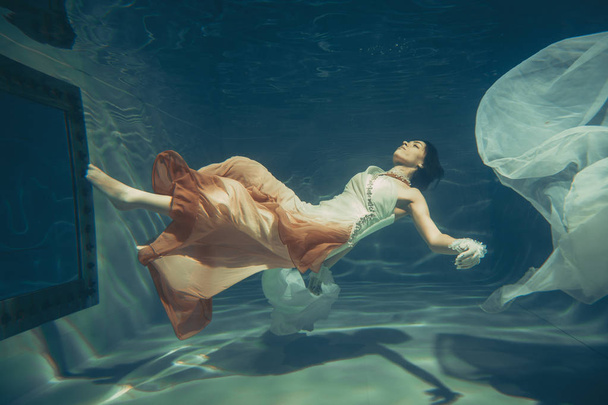 elegante menina delgada nada debaixo d 'água como um mergulhador livre em um vestido de noite branco com belo tecido
 - Foto, Imagem