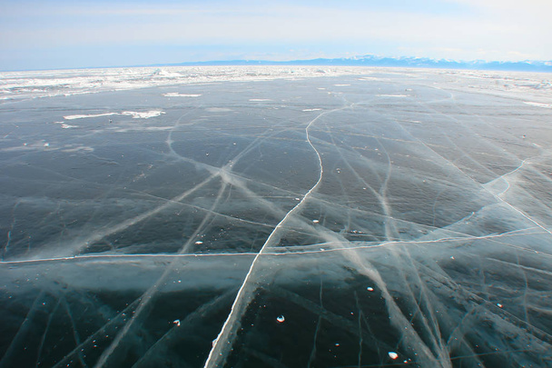 paysage hivernal avec lac gelé ; épaisse glace bleu foncé fissurée ; fissures extérieures et intérieures ; rivage rocheux éloigné ; ciel matinal dans la brume givrée ; plan grand angle
 - Photo, image