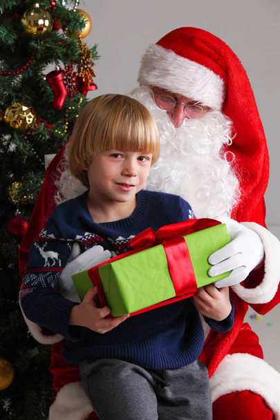 Portrait of smiling little boy sitting on santa claus knees and getting a gift - Foto, immagini