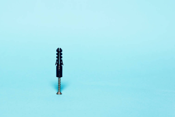 A metal screw screwed into a black peg on a pastel blue background. The concept of minimalism. - Фото, изображение