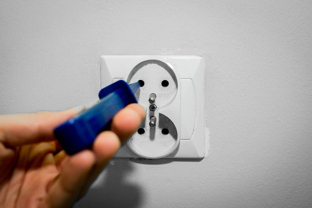 Tournevis bleu dans une prise électrique. L'électricien vérifie si le courant circule dans la prise à l'aide d'un tournevis avec un débitmètre de courant
. - Photo, image