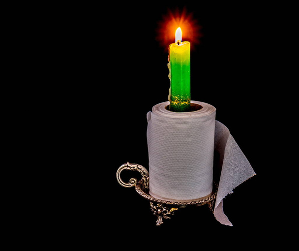 A silver candle holder with a burning candle and a roll of toilet paper isolated on a black background image with copy space in landscape format - Photo, Image