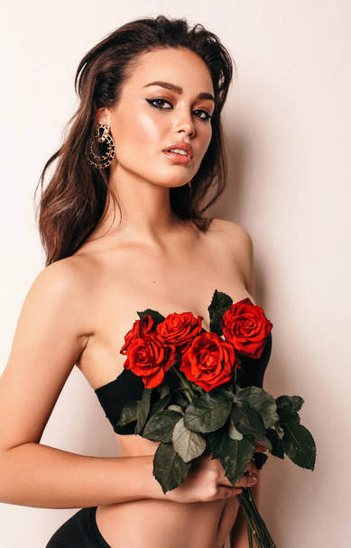 fashion studio photo of beautiful sexy woman with dark hair in elegant lingerie, holding bouquet of roses in hands - Photo, image