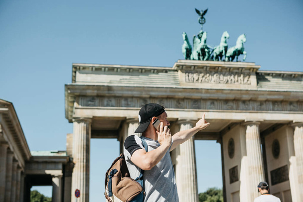 Egy turista vagy egy srác egy hátizsák mobiltelefonon beszél, és megmutatja a kezét, a Brandenburgi kapu Berlinben - Fotó, kép