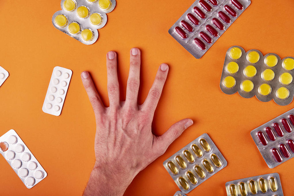 Člověk si vybere lék pro léčbu. Mužské ruky na oranžové pozadí a spoustu různých pilulky, léky, vitamíny, minerály, potravinářské přídatné látky. Doktor se snaží udělat diagnózu. - Fotografie, Obrázek