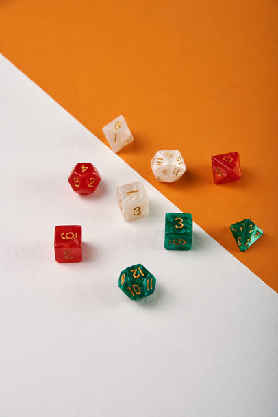 ungewöhnliche Würfel für Brettspiele auf zweifarbigem weißem und orangefarbenem Hintergrund, Tisch. Zubehör, Kieselsteine, Würfel für das berühmte Brettspiel "Dungeons and Dragons"". - Foto, Bild