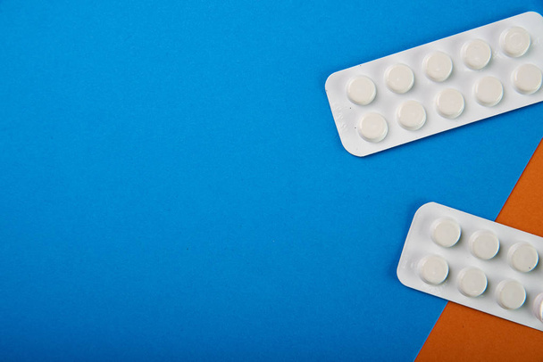 eine Packung schlichter weißer Pillen auf zweifarbigem blau-orangefarbenem Hintergrund. Medikamente in der pharmazeutischen Verpackung. illegale Verteilung von Betäubungsmitteln durch Drogenhändler. Medikamententherapie vom Therapeuten. - Foto, Bild