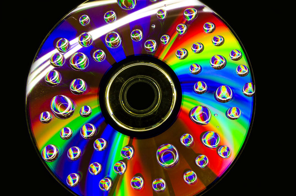 Primer plano de gotas de agua en una superficie multicolor con un hermoso reflejo en la superficie de un disco compacto
. - Foto, imagen