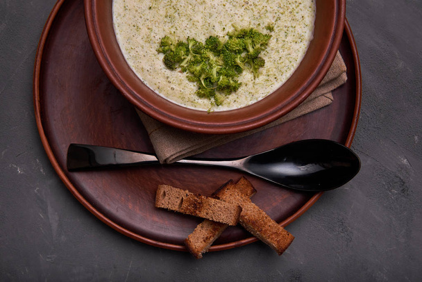 Heerlijke broccoli crème soep in een mooi klei kom. Soep-puree en kleine toast van roggebrood. Prachtige zwarte eethoek lepel en een servet grof doek. Gastronomisch restaurant lunch. - Foto, afbeelding