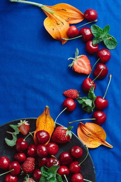 Ripe, fresh sweet cherry and berries in black plate on blue  background.  Healthy diet. Top view, copy space. Place for text. - Foto, Imagen