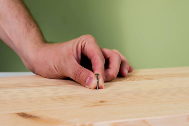 Een nagel hameren in houten plaat. Concept van renovatie, huishoudelijk werk. De man houdt een blauwe hamer in zijn hand, met een nagel in de andere hand. Klusjesman, Diy. - Foto, afbeelding