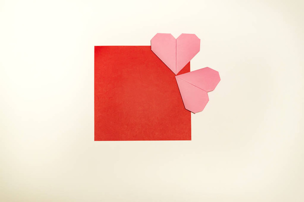 Greeting card for Valentine's Day from pink handcraft of origami hearts presented on a red frame on a white background with copy space. Top view - Photo, image