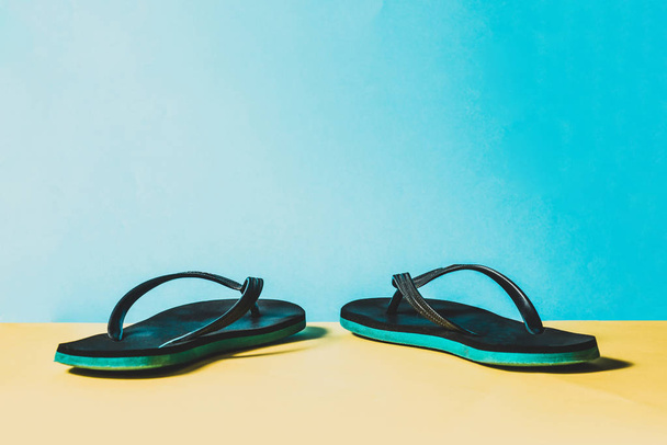 Zwarte en groene slippers, zomer set. De zomer is komende concept. Minimalistische stijl, minimalistische fotografie. Geel, roze en blauw pastel kleuren achtergrond. - Foto, afbeelding