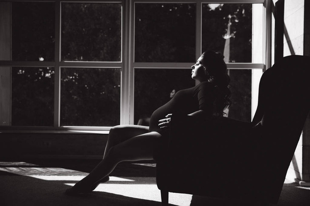 Beautiful pregnant woman sit on the chair in front of big window - Fotó, kép
