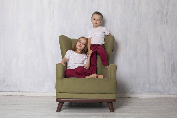 kleine jongen en meisje zijn broer en zus zitten op een groene stoel - Foto, afbeelding