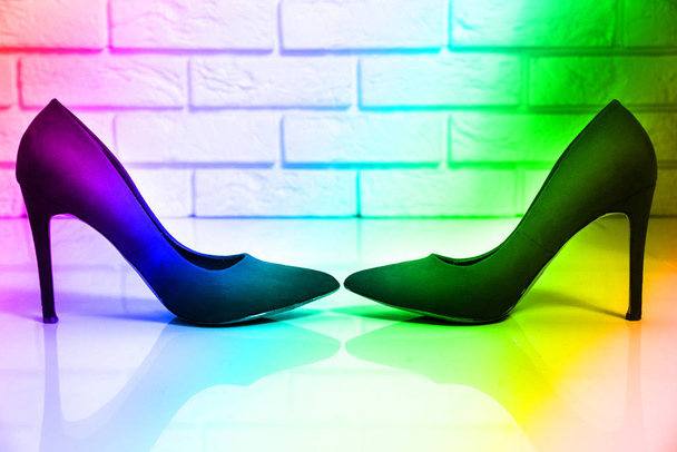 Bunte High Heels. Zwei High Heels von Frauen stehen auf einem hellen Fußboden, eine weiße Backsteinwand steht einander gegenüber. Regenbogen, helle Farben. - Foto, Bild