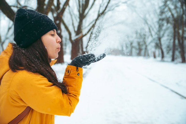 Kobieta dmuchanie śniegu z jej rąk. zasypani park na tle. koncepcja sezon zimowy - Zdjęcie, obraz