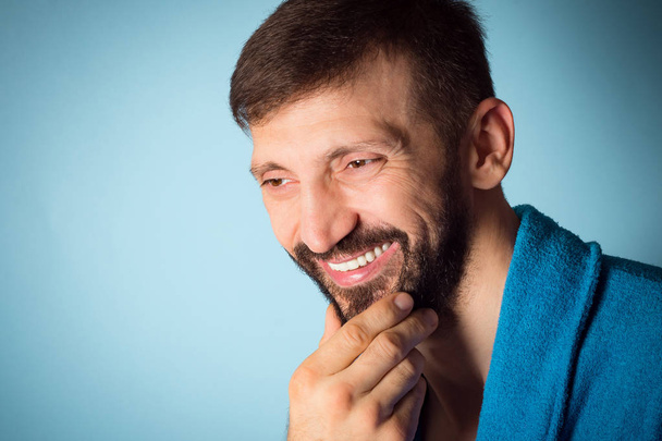 Beauty portrait of smiling handsome middle aged bearded man on blue background, cosmetics for men and male beauty concept. - Фото, изображение