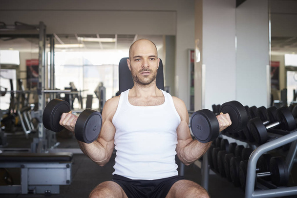 Shot of man in the gym doing dumbbell exercises to create more muscular body. - Foto, afbeelding