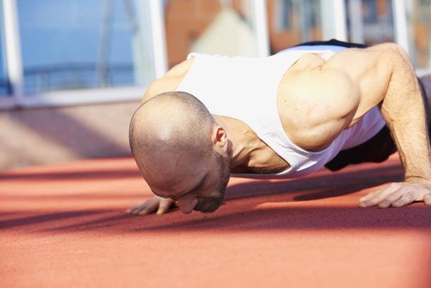 Shot de atleta hombre haciendo flexiones durante el entrenamiento al aire libre
.  - Foto, Imagen