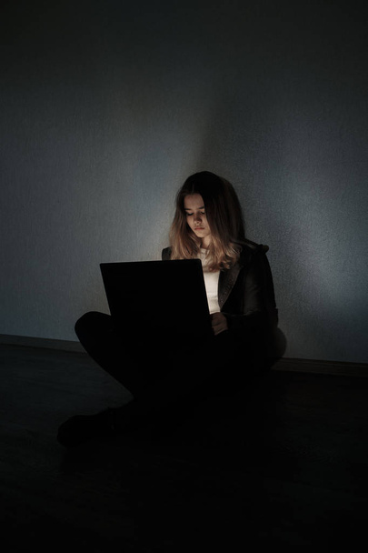 暗い部屋でノート パソコンのそばに座って悲しい十代の少女。彼女はオンラインいじめストーカー社会の犠牲者です。 - 写真・画像
