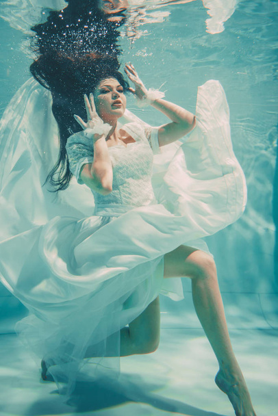 sexy young bride swimming underwater in white wedding dress, stockings and gloves - Photo, Image