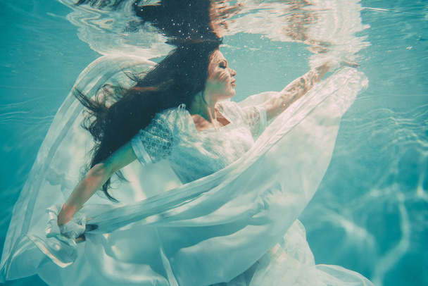 sexy junge Braut schwimmt unter Wasser in weißem Brautkleid, Strümpfen und Handschuhen - Foto, Bild