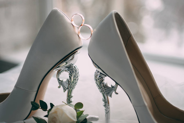 Um par de sapatos de casamento brancos com anéis em um banquinho
 - Foto, Imagem
