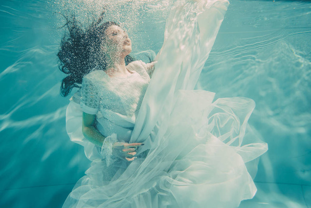 sexy young bride swimming underwater in white wedding dress, stockings and gloves - Photo, image