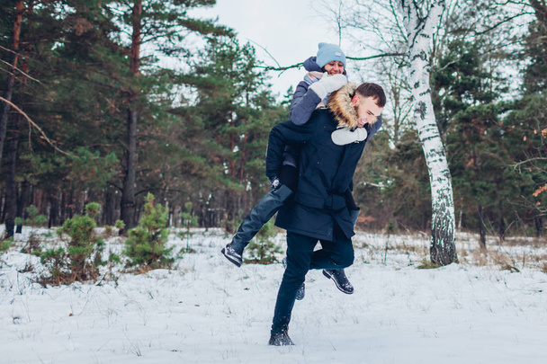 Kaveri antaa tyttöystävänsä reppuselässä talvimetsässä. Rakastava pariskunta pitää hauskaa ulkona. Onnelliset ihmiset rentoutuvat
 - Valokuva, kuva