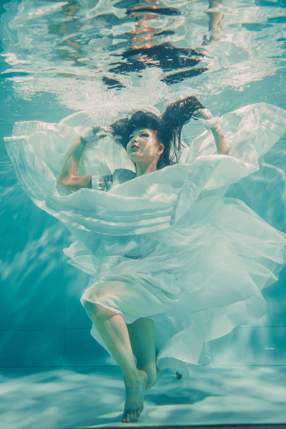 σέξι νεαρή νύφη υποβρύχια κολύμβηση σε λευκό νυφικό φόρεμα, κάλτσες και γάντια - Φωτογραφία, εικόνα