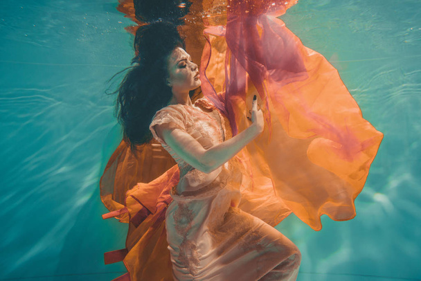 girl with orange dress is dreamy and meditative floating under water, like the soul before reincarnation - Photo, Image