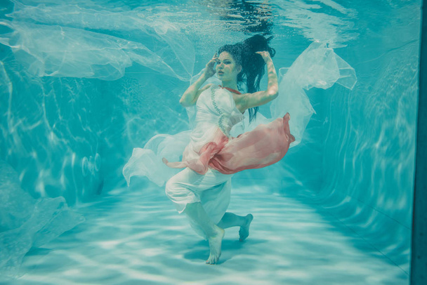mooi model meisje onderwater zwemmen in vrouwelijke lange witte en roze jurk - Foto, afbeelding