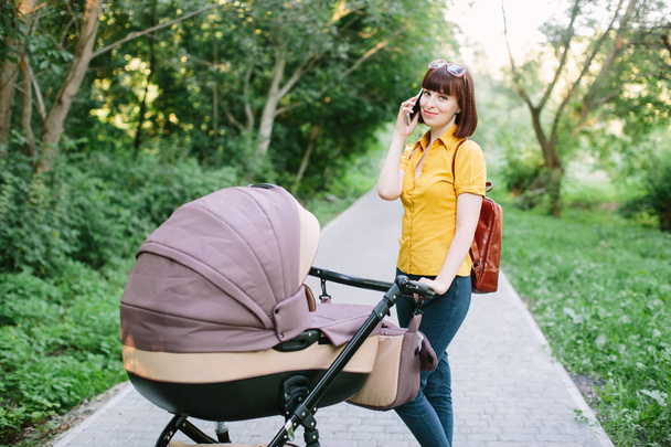 Full length portrait of a mother talking on the phone with a stroller. Young mom - Foto, Imagen