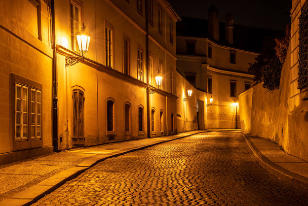 Narrow cobbled street in old medieval town with illuminated houses by vintage street lamps, Novy svet, Prague, Czech Republic. Night shot - Photo, Image