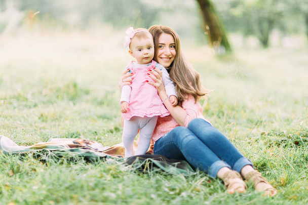 Happy mother and daughter in the park. Beauty nature scene with family outdoor lifestyle. Happy family resting together on the green grass, having fun outdoor. Happiness and harmony in family life. - Φωτογραφία, εικόνα