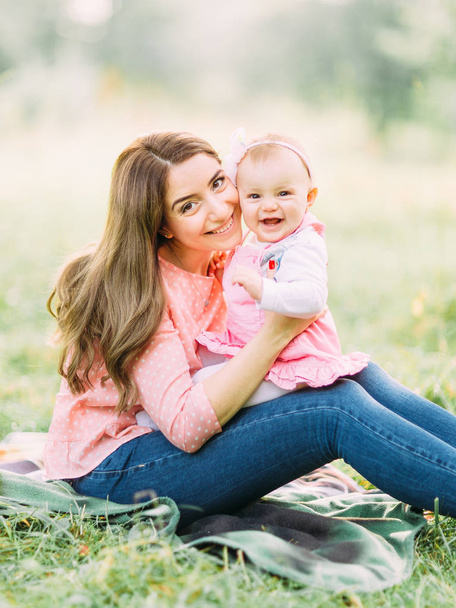 Happy mother and daughter in the park. Beauty nature scene with family outdoor lifestyle. Happy family resting together on the green grass, having fun outdoor. Happiness and harmony in family life. - Foto, Imagen