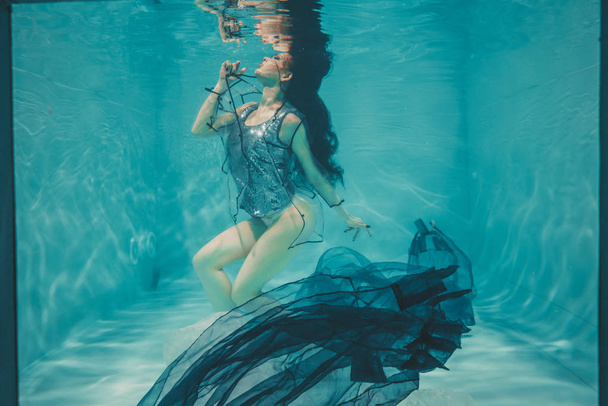piękny model dziewczyna pływa pod wodą w t-shirt szary cekinami i przejrzyste modny płaszcz PCV - Zdjęcie, obraz