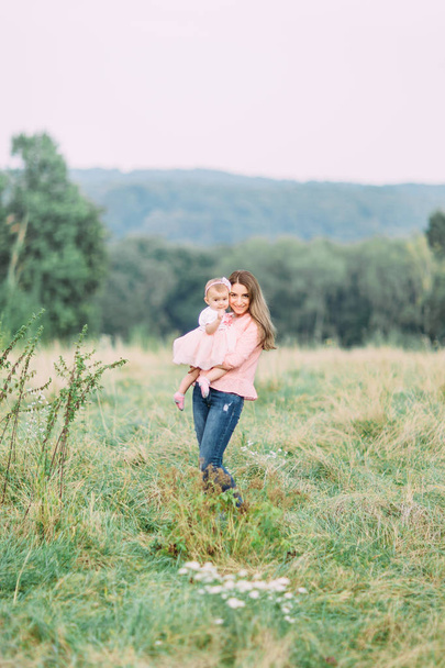 Mother and little daughter playing together in a park. Happy cheerful family. Mother and baby kissing, laughing and hugging in nature outdoors - 写真・画像