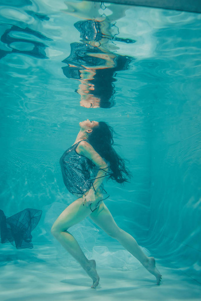 mooi model meisje zwemt onder water in een t-shirt in grijze pailletten en een transparante regenjas voor trendy Pvc - Foto, afbeelding
