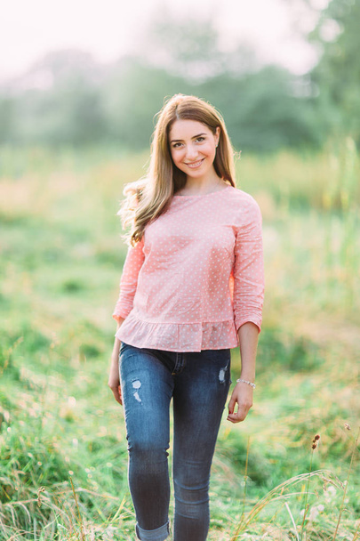 Beauty young girl outdoors enjoying nature. Fashion young woman in pink shirt and jeans in meadow - Foto, Imagen