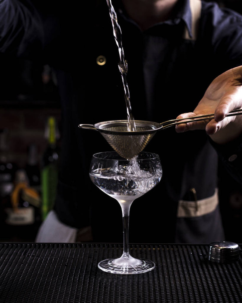 Бармен делает освежающий коктейль на фоне бара. Темный капризный стиль. Лёд в стакане
 - Фото, изображение