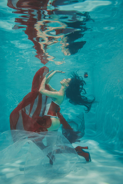 hermosa chica sexy nadando bajo el agua en estilo deportivo rojo y blanco fetiche corsé y sobre la rodilla botas altas muslo con tacones
 - Foto, imagen