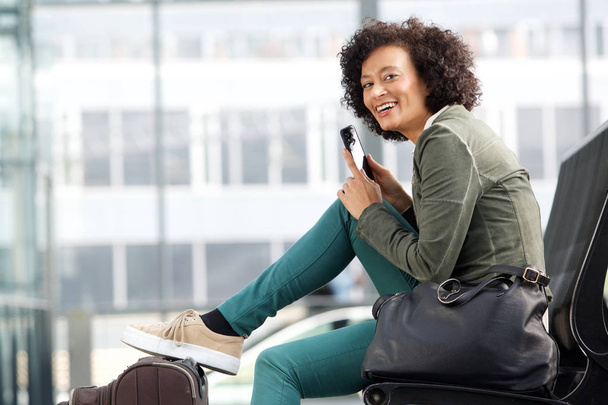 Portret van de kant van Afro-Amerikaanse vrouw zitten op bankje met cellphone - Foto, afbeelding