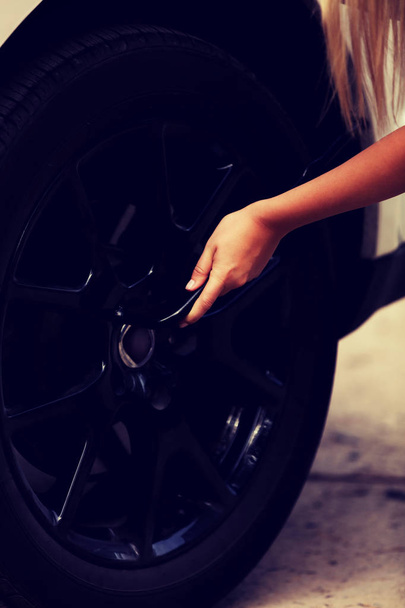 Woman is changing tire of car with wheel wrench - Foto, Imagen