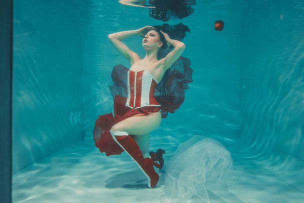 schöne sexy Mädchen schwimmen unter Wasser in sportlichem Stil rot-weißen Fetisch Korsett und über Knie Oberschenkel hohe Stiefel mit Fersen - Foto, Bild