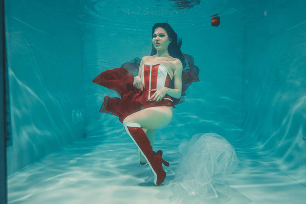 szép szexi lány, víz alatti úszás, sportos stílus piros és fehér fetish fűző és a térd felett comb magas sarkú csizma - Fotó, kép