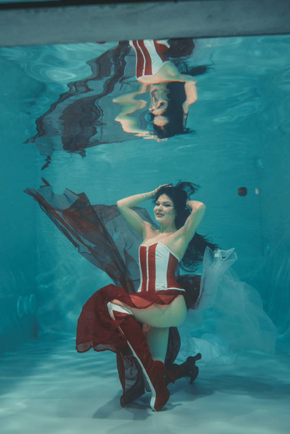 kaunis seksikäs tyttö uinti vedenalainen urheilullinen tyyli punainen ja valkoinen fetissi korsetti ja yli polvi reiteen korkeat saappaat korkokengät
 - Valokuva, kuva