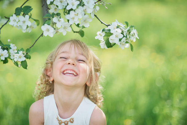 Cute little girl sniffing flowers of apple orchard. Garden with flowering trees. Allergy season - Photo, Image
